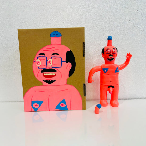 Neon pink painted soft vinyl figure of a nude man with glasses. He is balding with some facial hair and has a blue tipped penis atop his head. His nipples are blue and his own penis is also blue tipped. One of his hands is formed into a peace sign.