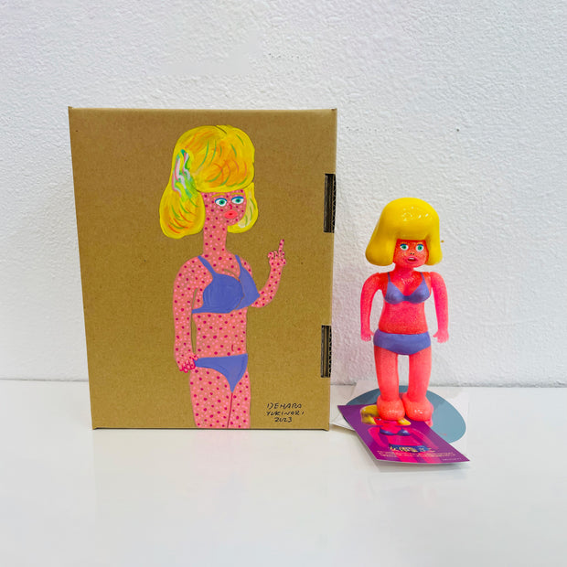 Neon pink soft vinyl figure of a woman in a purple bikini, with large puffed blonde hair. She stands next to a painted box.