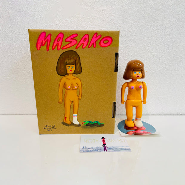Tan soft vinyl figure of a woman naked except for one tube sock, with large puffed brown hair. She stands next to a painted box.