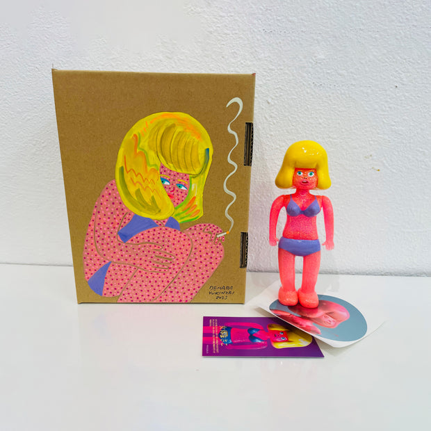 Neon pink soft vinyl figure of a woman in a purple bikini, with large puffed blonde hair. She stands next to a painted box.