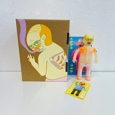 Semi translucent soft vinyl figure of a business man, shirtless in light pink slacks. He stands next to a painted box.