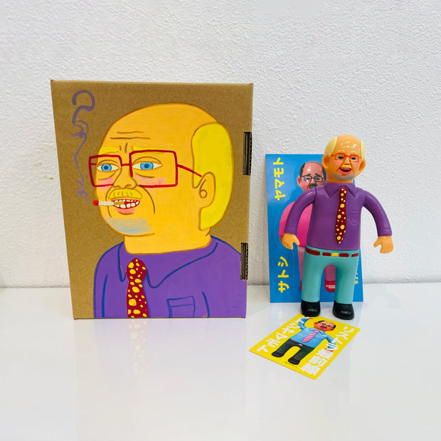 Soft vinyl figure of a business man wearing a bright purple button up and blue slacks. He stands next to a painted box.