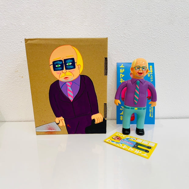 Soft vinyl figure of a business man wearing a light purple button up and blue slacks. He stands next to a painted box.