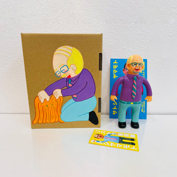 Soft vinyl figure of a business man wearing a light purple button up and blue slacks. He stands next to a painted box.