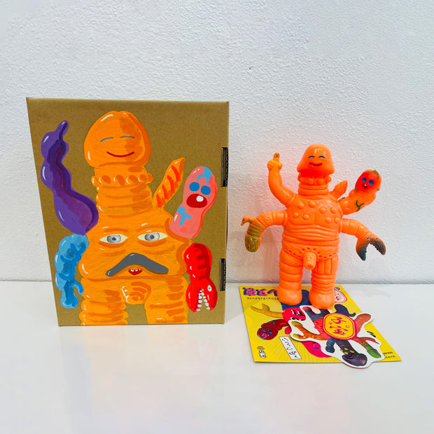 Orange soft vinyl figure of a creature with many arms, mostly penis shaped along with a claw and a human hand, jutting out of its body. It stands next to a painted box.