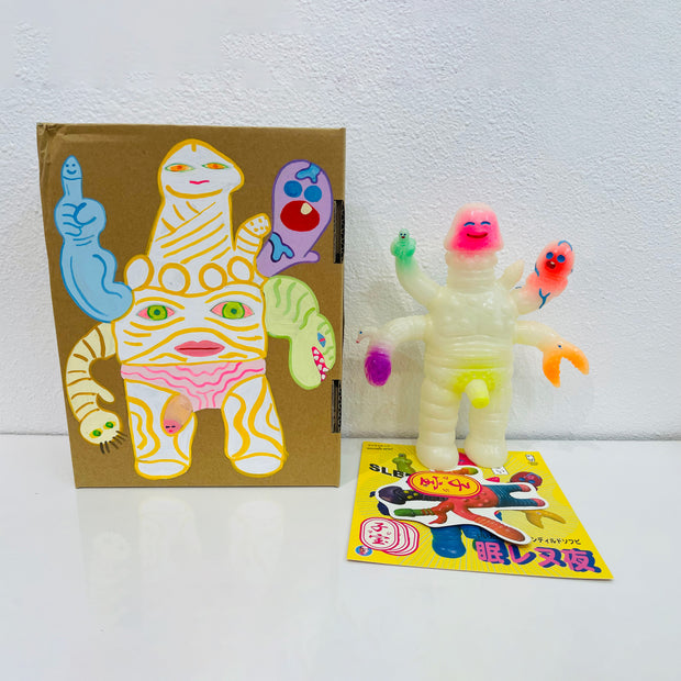Light yellow soft vinyl figure of a creature with many multicolor arms, mostly penis shaped along with a claw and a human hand, jutting out of its body. It stands next to a painted box.