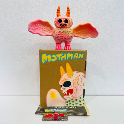Soft vinyl figure of a creature that looks part bat, part moth. It is light pink and dotted all over. It stands atop of a painted box.