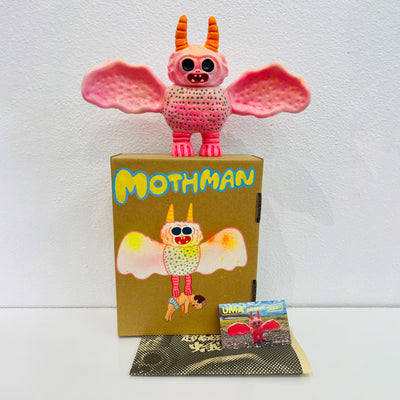 Soft vinyl figure of a creature that looks part bat, part moth. It is light pink and dotted all over. It stands atop of a painted box.
