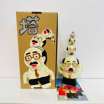 Glow in the dark colored vinyl figure of a short, stout business man. Atop his head are 4 other heads similar to his own, each one smaller then the next, building a tower of sorts. It stands in front of its product packaging.