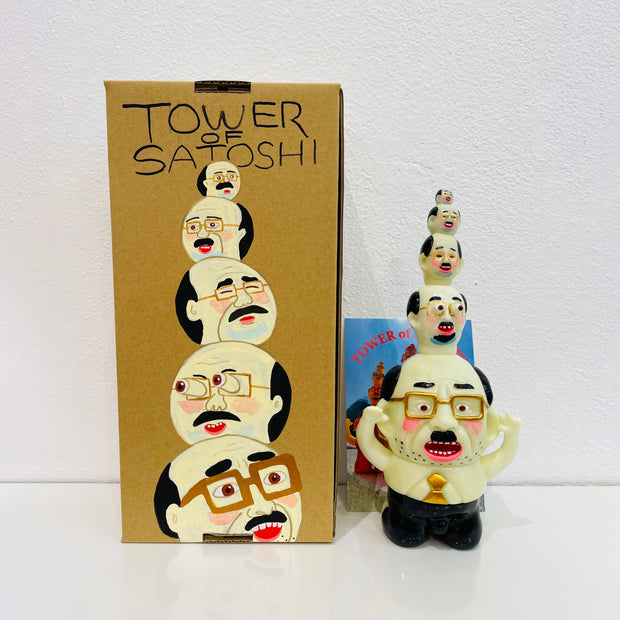 Glow in the dark colored vinyl figure of a short, stout business man. Atop his head are 4 other heads similar to his own, each one smaller then the next, building a tower of sorts. It stands in front of its product packaging.