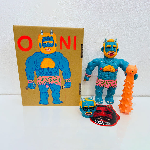 Blue soft vinyl figure of a demon man, with muscles and horns atop his head. He has a large orange spiked club and a human head at his feet. He stands next to a painted box.