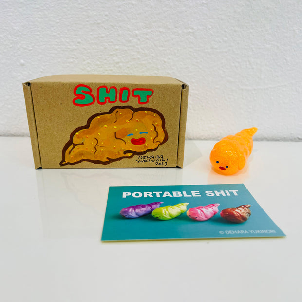 Small semi transparent orange figurine shaped like a poop. It sits next to a painted box.