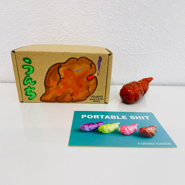 Small orangish brown figurine shaped like a poop. It sits next to a painted box.
