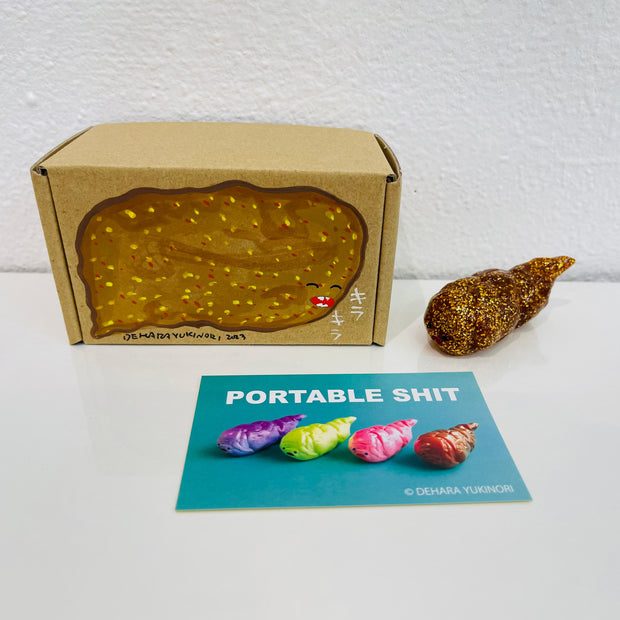 Small glittery gold figurine shaped like a poop. It sits next to a painted box.