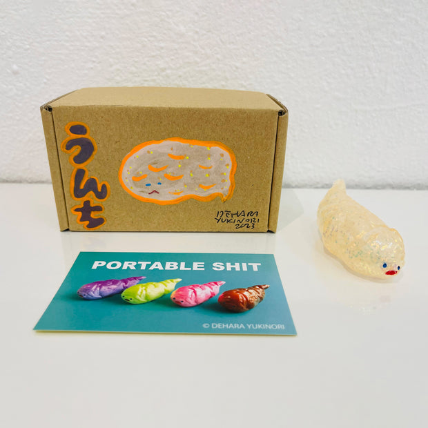 Small semi transparent glittery white figurine shaped like a poop. It sits next to a painted box.