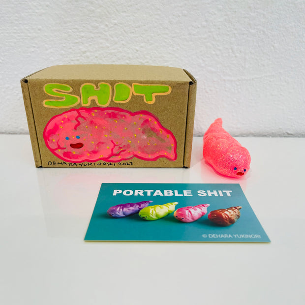 Small semi transparent glittery pink figurine shaped like a poop. It sits next to a painted box.