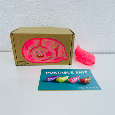 Small semi transparent glittery pink figurine shaped like a poop. It sits next to a painted box.