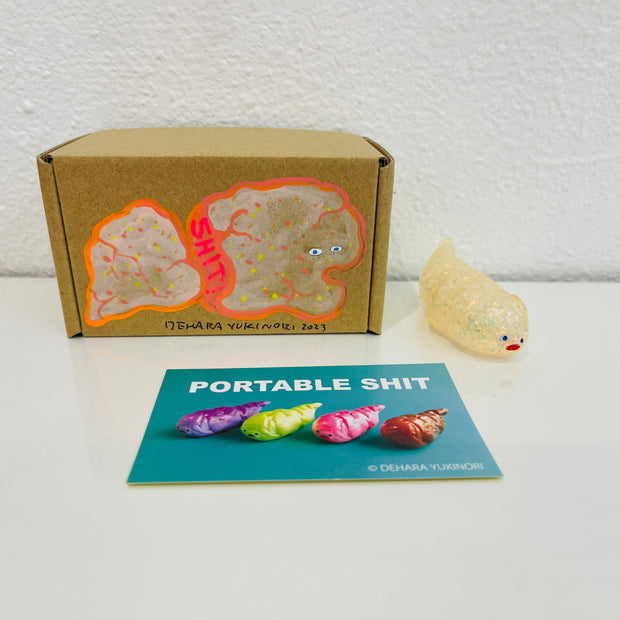 Small semi transparent glittery cream figurine shaped like a poop. It sits next to a painted box.