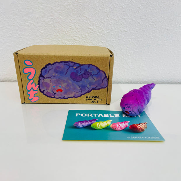 Small pinkish purple figurine shaped like a poop. It sits next to a painted box.