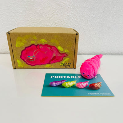 Small pink figurine shaped like a poop. It sits next to a painted box.