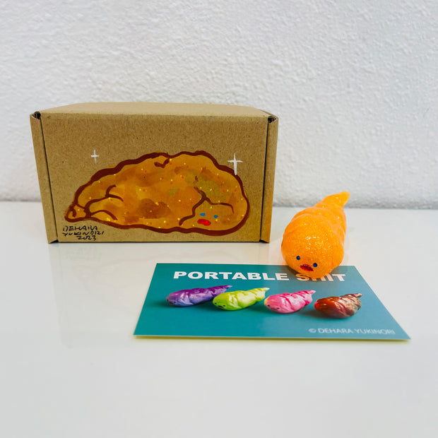 Small semi transparent glittery orange figurine shaped like a poop. It sits next to a painted box.