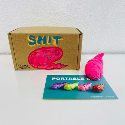 Small pink figurine shaped like a poop. It sits next to a painted box.
