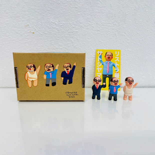 Set of 3 small vinyl figures of little business men. One wears a suit, another wears a tie over a t-shirt and the other wears underwear. They stand next to a painted box.