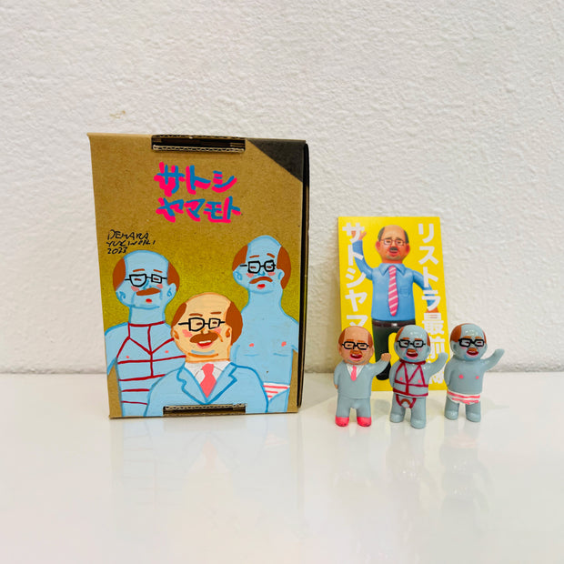  Set of 3 small vinyl figures of little business men. One wears a suit, another wears a red bondage wear and the last wears striped underwear. They stand next to a painted box.
