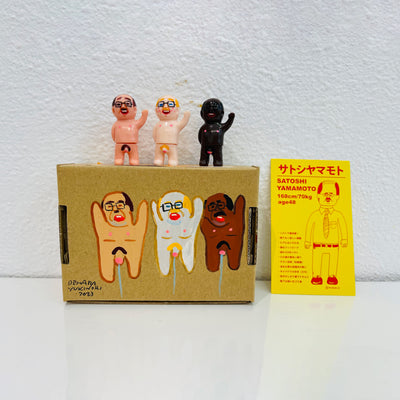 Set of 3 small vinyl figures of little business men. They are all nude and are of differing skin tones. They stand next to a painted box.