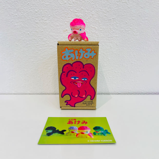Small pink soft vinyl figure of an octopus creature, with a large head and small limbs. It stands on a painted box.