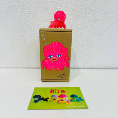 Small pink soft vinyl figure of an octopus creature, with a large head and small limbs. It stands on a painted box.