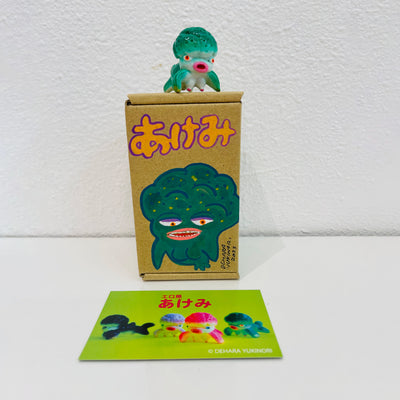 Small green soft vinyl figure of an octopus creature, with a large head and small limbs. It stands on a painted box.