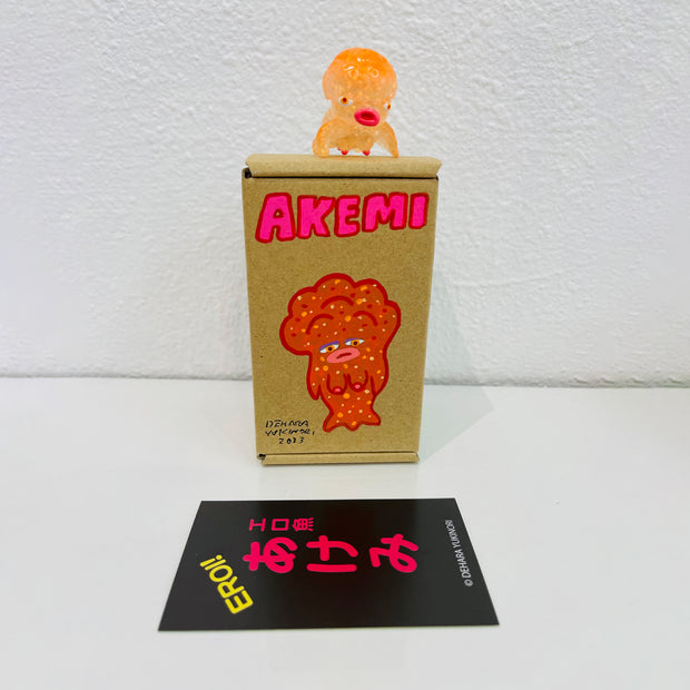 Small semi transparent orange soft vinyl figure of an octopus creature, with a large head and small limbs. It stands on a painted box.