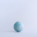 Small blue round bottomed jar with a lid. The lid has a slightly pointed tip wit white coloring and a drawn on, cute face. 