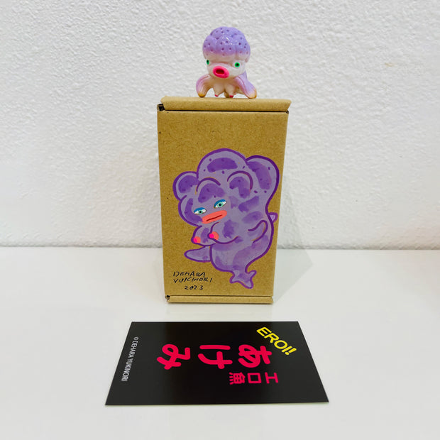 Small purple soft vinyl figure of an octopus creature, with a large head and small limbs. It stands on a painted box.