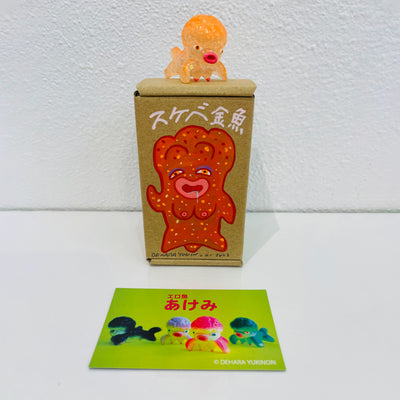 Small semi transparent orange soft vinyl figure of an octopus creature, with a large head and small limbs. It stands on a painted box.