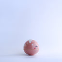 Small pink round bottomed jar with a lid. The lid has white coloring at the very top and a drawn on, cute face with rosy cheeks.