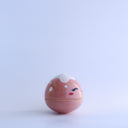 Small pink round bottomed jar with a lid. The lid has white coloring at the very top and a drawn on, cute face with rosy cheeks.