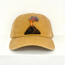 A muted yellow baseball cap featuring a small embroidered volcano patch on the front, set against a plain white background.