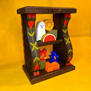 Decorative wooden shelf with colorful floral themed paintings along the side. Small, cute wooden characters are on the shelves like trinkets.