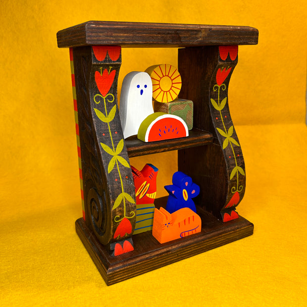 Decorative wooden shelf with colorful floral themed paintings along the side. Small, cute wooden characters are on the shelves like trinkets.