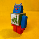Colorful toy robot with a turtle design on its chest against a yellow background