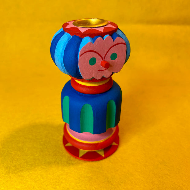 Colorful wooden candle holder with a face on a yellow background
