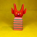 Colorful wooden toy figure with a red, cute devil character with a striped body on a yellow background