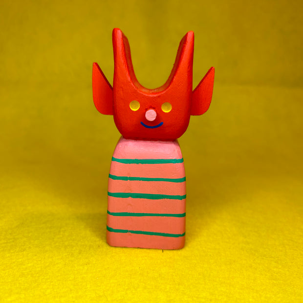 Colorful wooden toy figure with a red, cute devil character with a striped body on a yellow background