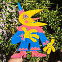 Die cut wooden sculpture of a yellow moon man, dressed like a clown in a blue and pink outfit and a small pointed hat.