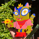 Colorful cat-shaped die cut wooden sculpture, painting like a green cowboy cat holding a raygun. Sculpture is held in a hand with a green leafy background