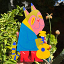 Die cut wooden sculpture of a pink cat creature wearing a blue jacket, red boots and holding a small guitar.