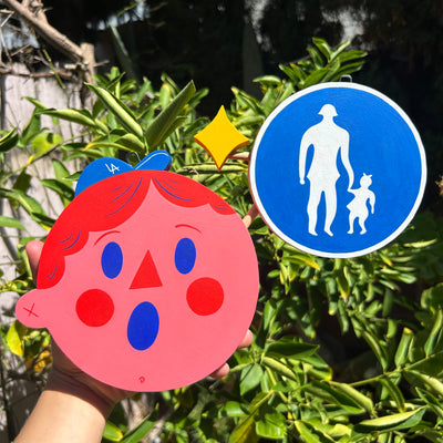 Die cut sculpture of a pink cartoon character's head, wearing a tiny LA cap with a surprised expression. Attached to him is a cross walk sign.