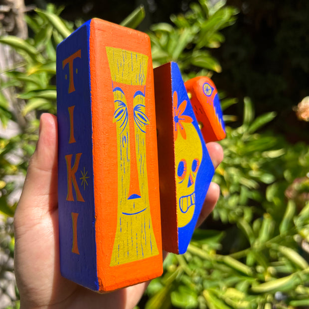 Wooden assemblage sculpture of a tiki bar sign with a tiki skull and a small bird.